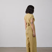 Person wearing a yellow checkered jumpsuit standing against a white wall.