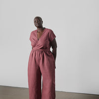 Person wearing a pink jumpsuit standing against a plain white wall.