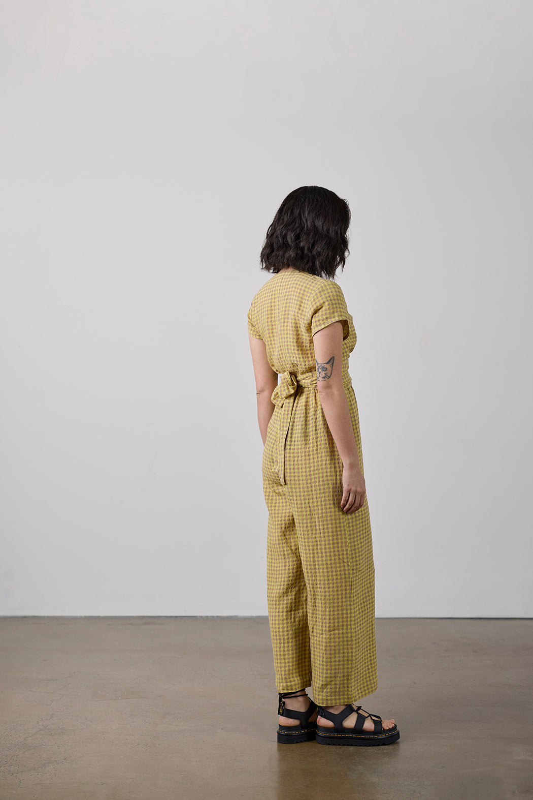 Person wearing a yellow checkered jumpsuit standing against a white wall.