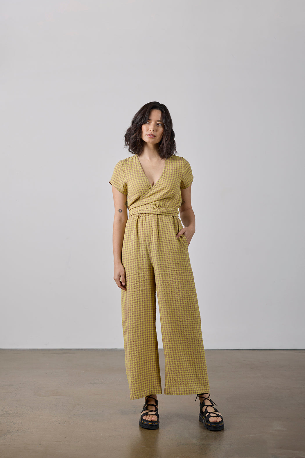 Woman wearing a yellow checkered jumpsuit against a plain background