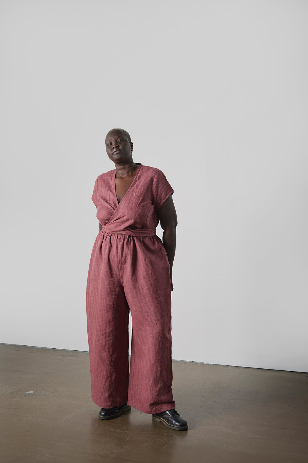 Person wearing a pink jumpsuit standing against a plain white wall.