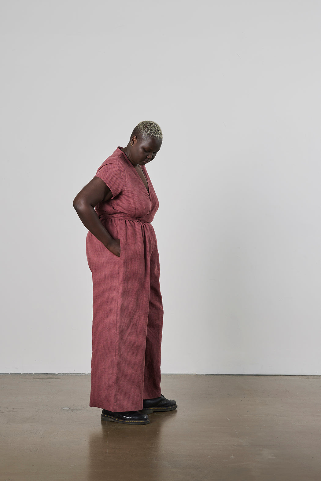 Person wearing a pink jumpsuit standing against a white wall with hand in their pocket.