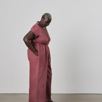 Person wearing a pink jumpsuit standing against a white wall with hand in their pocket.